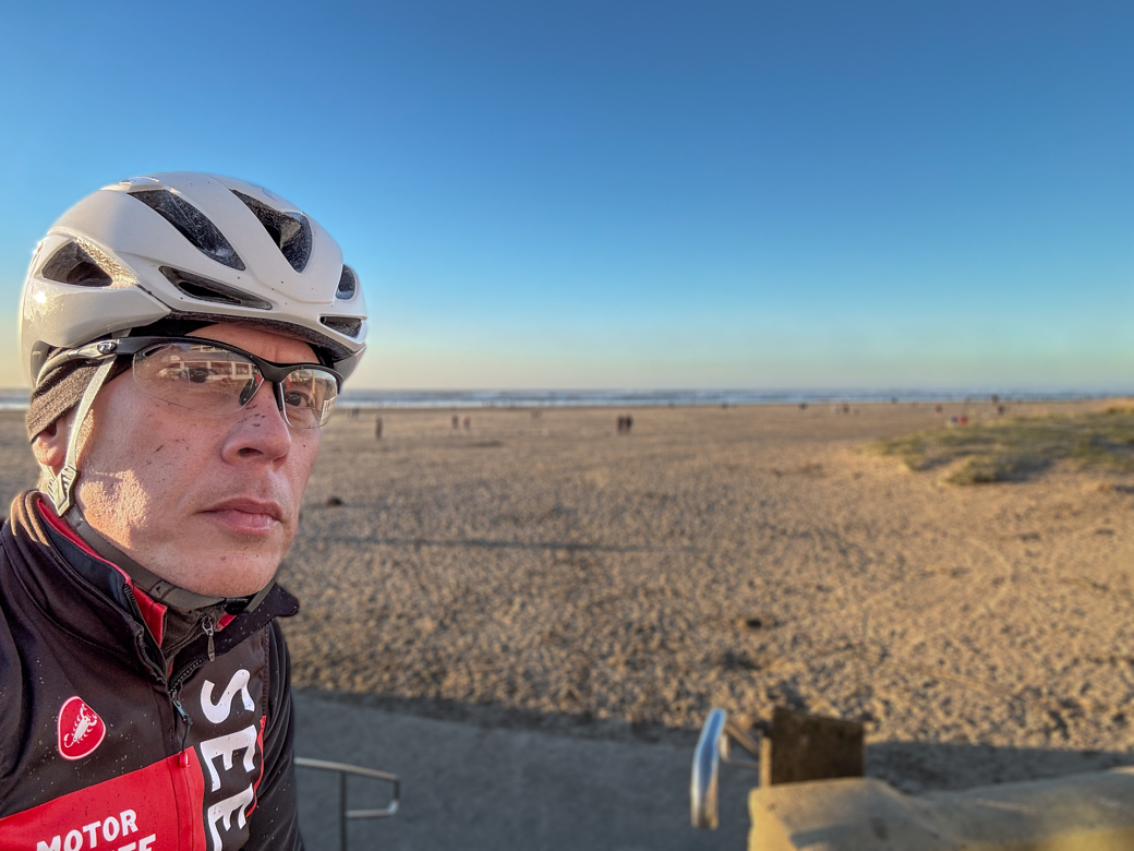 A man in a bike helmet taking a selfie at the beach.