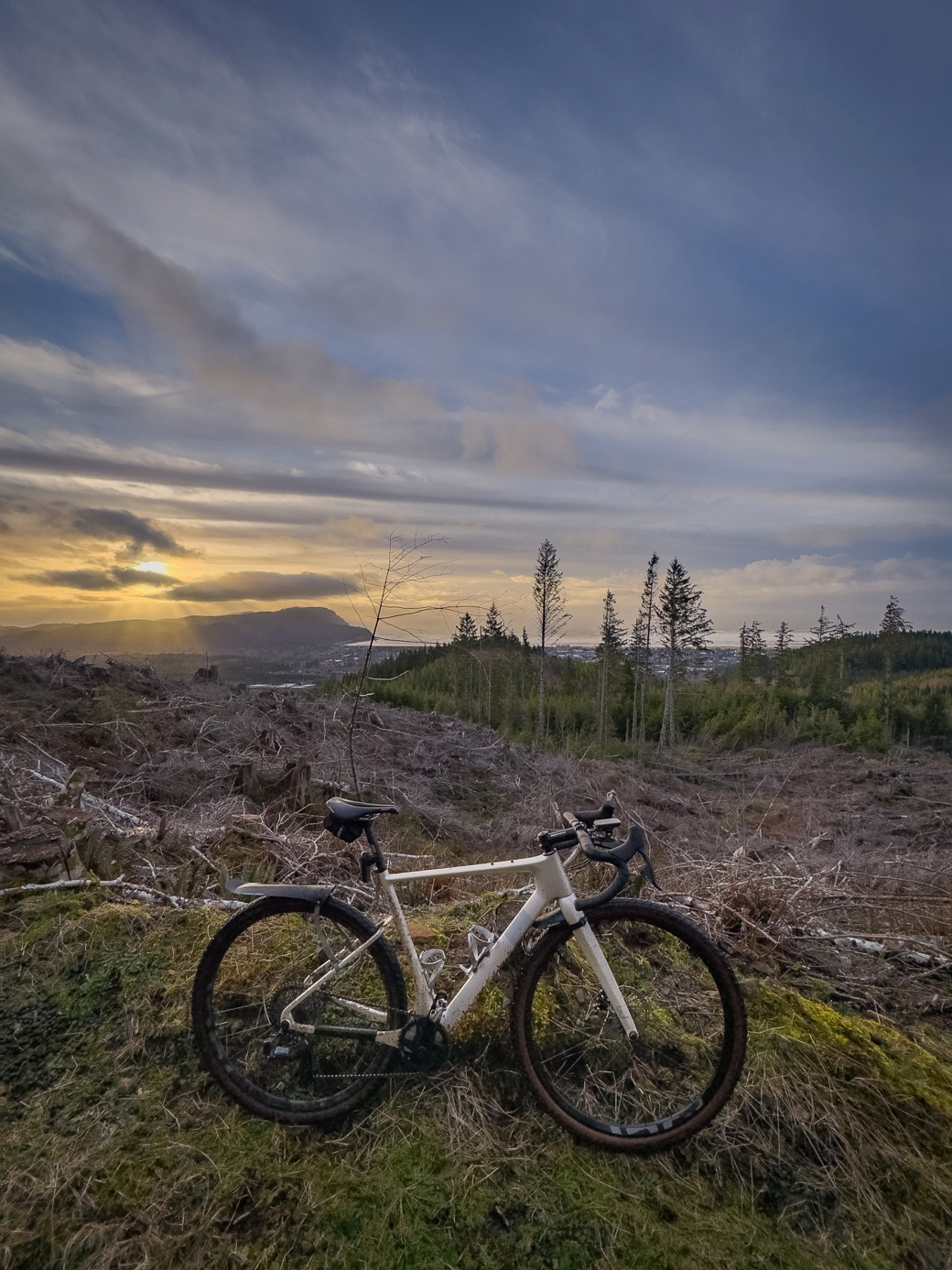 A bicycle is parked on a hill in front of a sunset.