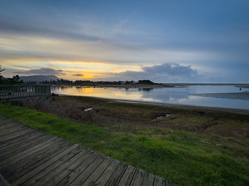 A wooden boardwalk overlooks a body of water at sunset.